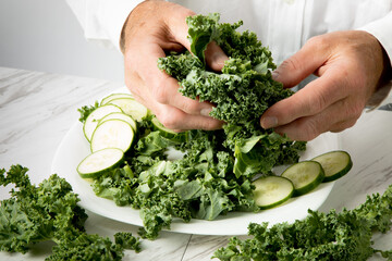 a chef holds cut up  kale leaves to be to be made into a massaged kale salad with cucumber slices...