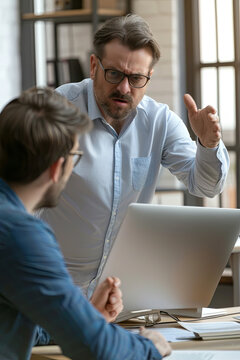 Angry boss criticizing scolding sad male employee for computer mistake incompetence at workplace, mad leader reprimanding rebuking shouting at subordinate lazy worker blaming of bad work in office
