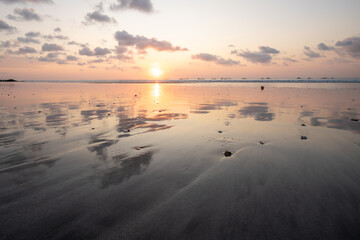 Fantastic sunset on the dream beach of Kuta, small waves setting over the sea and the reflection of the sky in the shallow water. News Bali in Indonesia