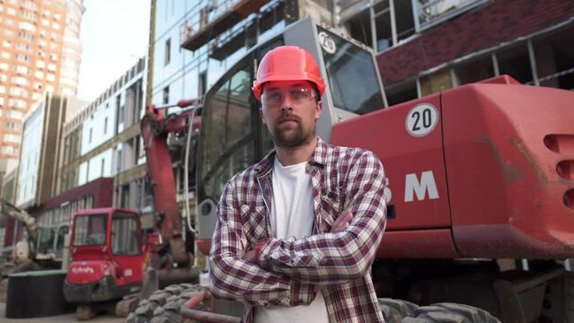 Portrait of proud builder at construction site. Constructor with excavator prepared to start building new house. Handsome construction worker standing in an outdoor area with heavy machinery. Engineer