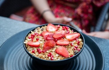 Breakfast granola with yogurt and strawberries on a black plate on a dark background