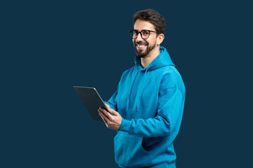 A man wearing a blue hoodie is holding a tablet device in his hands. He appears focused on the...