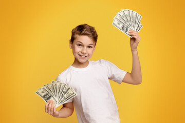 Saving money concept. Happy teen boy holding bunch of money, orange background