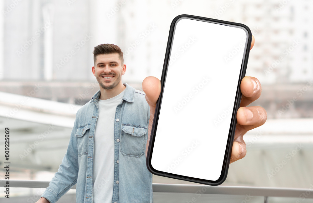 Poster A man is holding a smart phone with white blank screen in his hand. The background is neutral, focusing on the man and the technology in his hand.