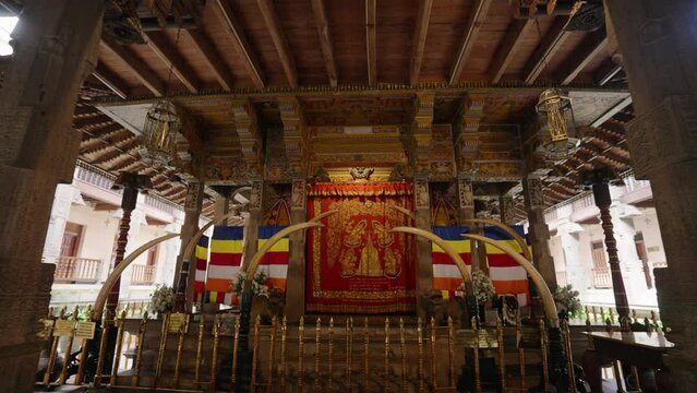 Interior of sacred Sri Dalada Maligawa, Temple of Tooth in Kandy. Golden Buddha, elaborate wood carvings, religious flags. Pilgrims visit, worship in ancient spiritual site. Rich cultural heritage.
