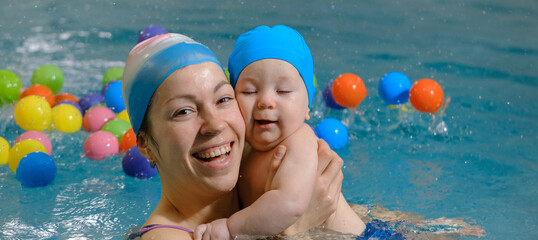 Banner Early swimming coach training to swim baby boy in indoor pool. Playing activity for infant...