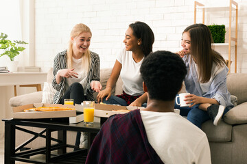 A small group of multiracial friends is seated around a coffee table in a well-lit living room,...