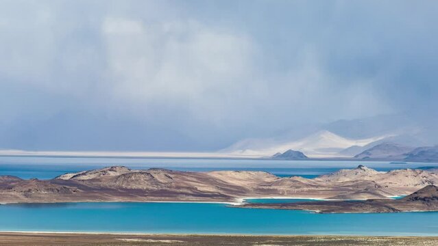 Tajikistan, Gorno-Badakhshan Autonomous Region (GBAO), Pamir Highway, panoramic view of sunny Karakul lake with grey clouds and storm over snowy mountains