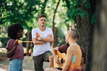 Young multicultural people having fun in park with guitar player.