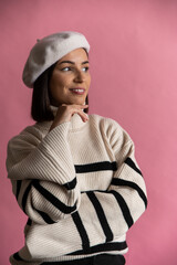 A woman in striped sweater and white beret smiles in front of pink background