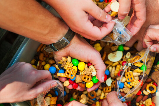 Kids hands fill plastic bags from a large container of trail mix