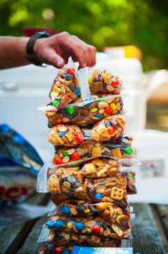 A hand stacks plastic bags of trail mix at a campsite