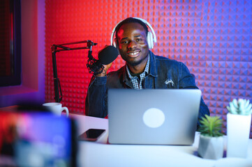 Young african american man recording or streaming podcast using microphone at his small broadcast...