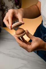 Girl's hands holding light brown macaron on a background with backlight