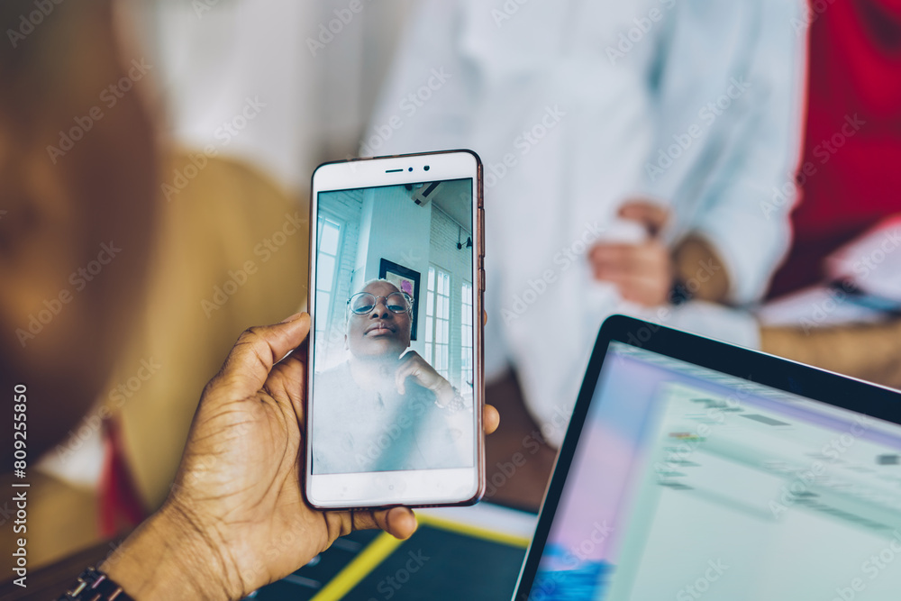 Poster cropped back view of young woman holding modern smartphone device in hands and talking via video cal