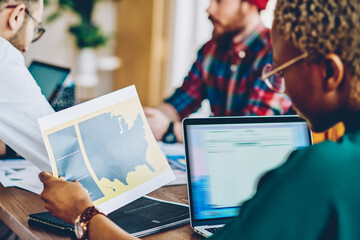 Smart female designer holding graphic illustration in hands while collaborating with colleagues...