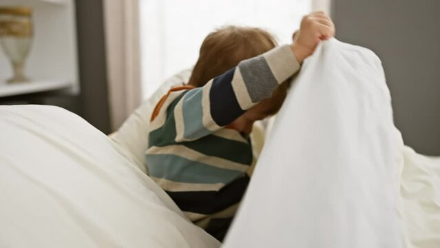 A cheerful toddler plays hide and seek under soft white sheets in a cozy bedroom setting, embodying innocence and childhood joy.