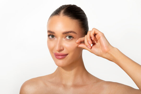 Young European woman touching her cheek and smiling at camera over white background. Cheek filler treatment, cheekbones lifting concept