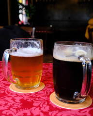 Two mugs of beer on a vibrant red tablecloth, one light and one dark, in a cozy pub atmosphere with soft background lighting.