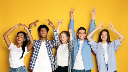 Five multiethnic teenagers stand side by side against a vibrant yellow backdrop, smiling and posing...