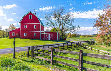 Fototapeta premium Bright red barn and split rail fence on farm. A red barn and white silo on the right side of it