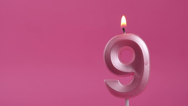 burning candle with number 9 on a pink background. Copy space. place for text.
