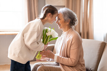 A young woman is tenderly presenting a bouquet of fresh white tulips to an elderly lady, who...