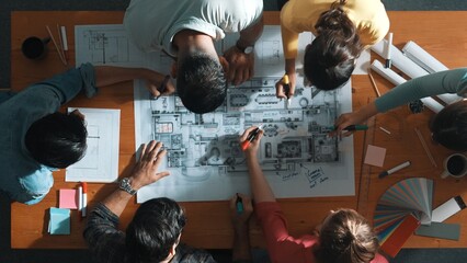 Top down view of civil engineer team writing at blueprint at meeting table with color palettes....