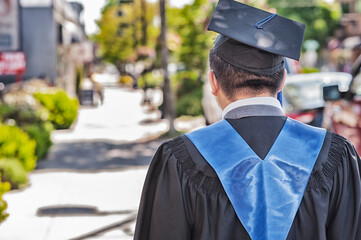 A recent male school successful graduate walks along sidewalk.