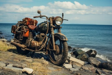 Obraz premium Old, rustic motorcycle with leather bags parked on a rocky beach with ocean backdrop