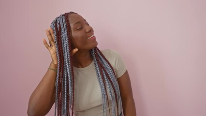 Cheerful african american woman, braids adorned, playfully eavesdropping on juicy gossip. hand cupping ear, basking in the secret rumors, oh the deafness of isolation on a pink backdrop!