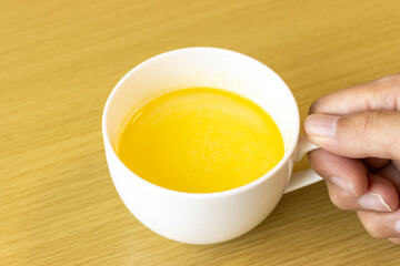 カップに入れたコーンスープを持つ男性の手