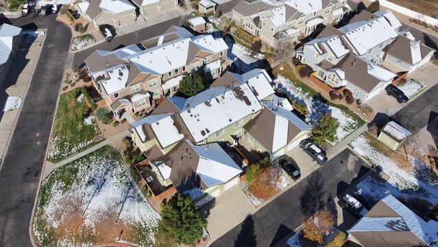 Aerial view of condominium homes in the morning after a snowstorm. Snow covers the condo complex's rooftops, grass, foliage, parked cars, and bushes. The complex is next to a busy highway.