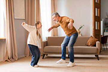 A cheerful grandfather engages in a playful dance with his young granddaughter in the warmth of...