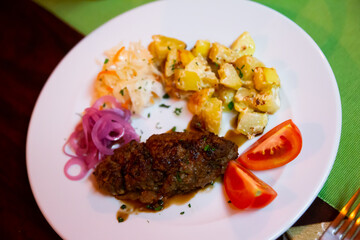 Plate with a meat dish lula-kebab, stewed potatoes, pickled cabbage, onions and slices of fresh...