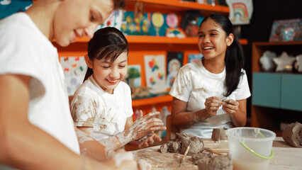 Caucasian highschool girl modeling cup of clay while looking smart boy in art class at workshop....