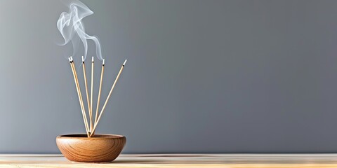 photo of incense sticks smoking in incense holder on table on solid background with copy space
