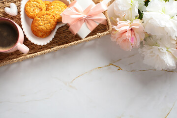 Top view cozy table with wicker tray with gift box, flowers, cup of coffee, cookies.