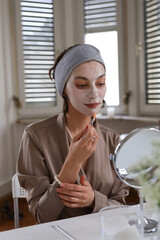 Woman in her room making facial mask holding mirror.Morning skin care routine.