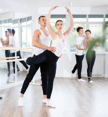 Obraz premium Happy ballet couple partners preparing in rehearsal for contest, training ballet poses with support in dance classroom
