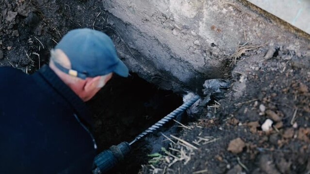 male worker drills the foundation with a hammer drill for sewerage in a country house.
