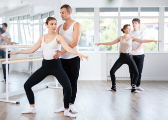 Positive ballet dancers couple performing graceful choreography, training demi plie ballet pose in modern gym or ballet hall