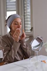 Woman Cleansing Skin With Micellar Water And Cotton Pad and looks in the mirror