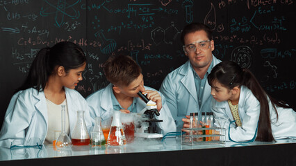 Multicultural student looking under microscope while cute girl inspect sample. Teacher looking...