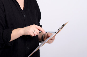 Close up of a blonde young woman in a black shirt pointing on a clipboard, grey studio background