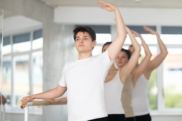 Motivated sporty young guy in white t-shirt and black sweatpants practicing balletic postures at...