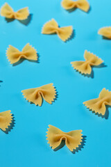 Naklejka premium Uncooked bow tie pasta, farfalle scattered on a blue background in a decorative pattern