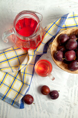 Plum Compote in jug with purple plums on white wooden background. .