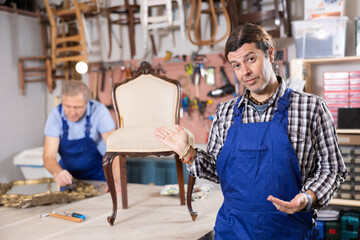 Middle-aged master restoration worker dressed in overalls poses in working atmosphere of his...
