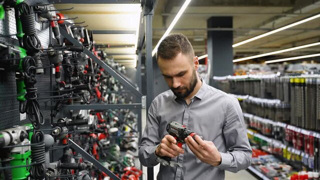 A man in a hardware store chooses a new screwdriver or drill